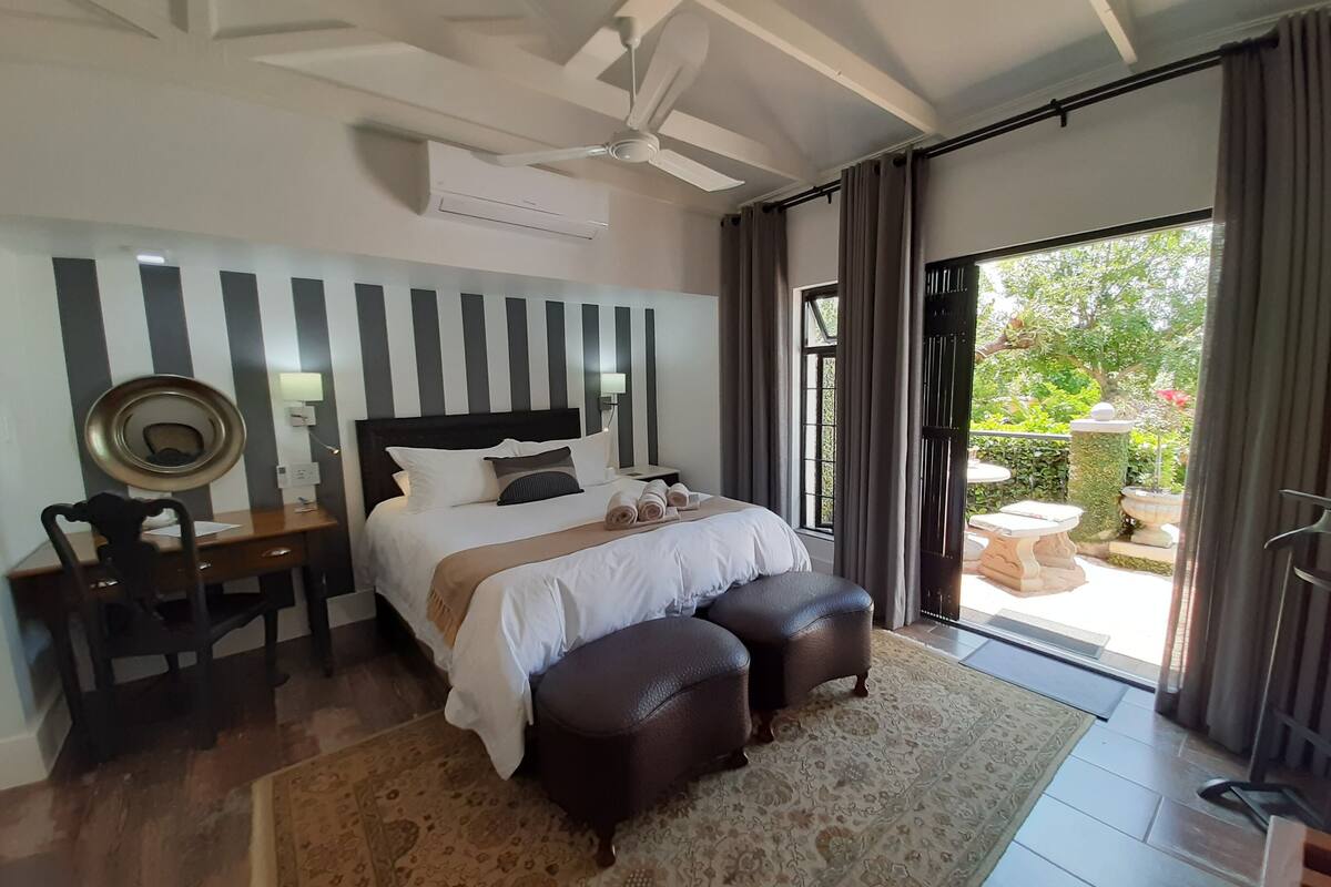 A hotel room with a bed, a desk, a chair, a ceiling fan, and a view of the outdoors.