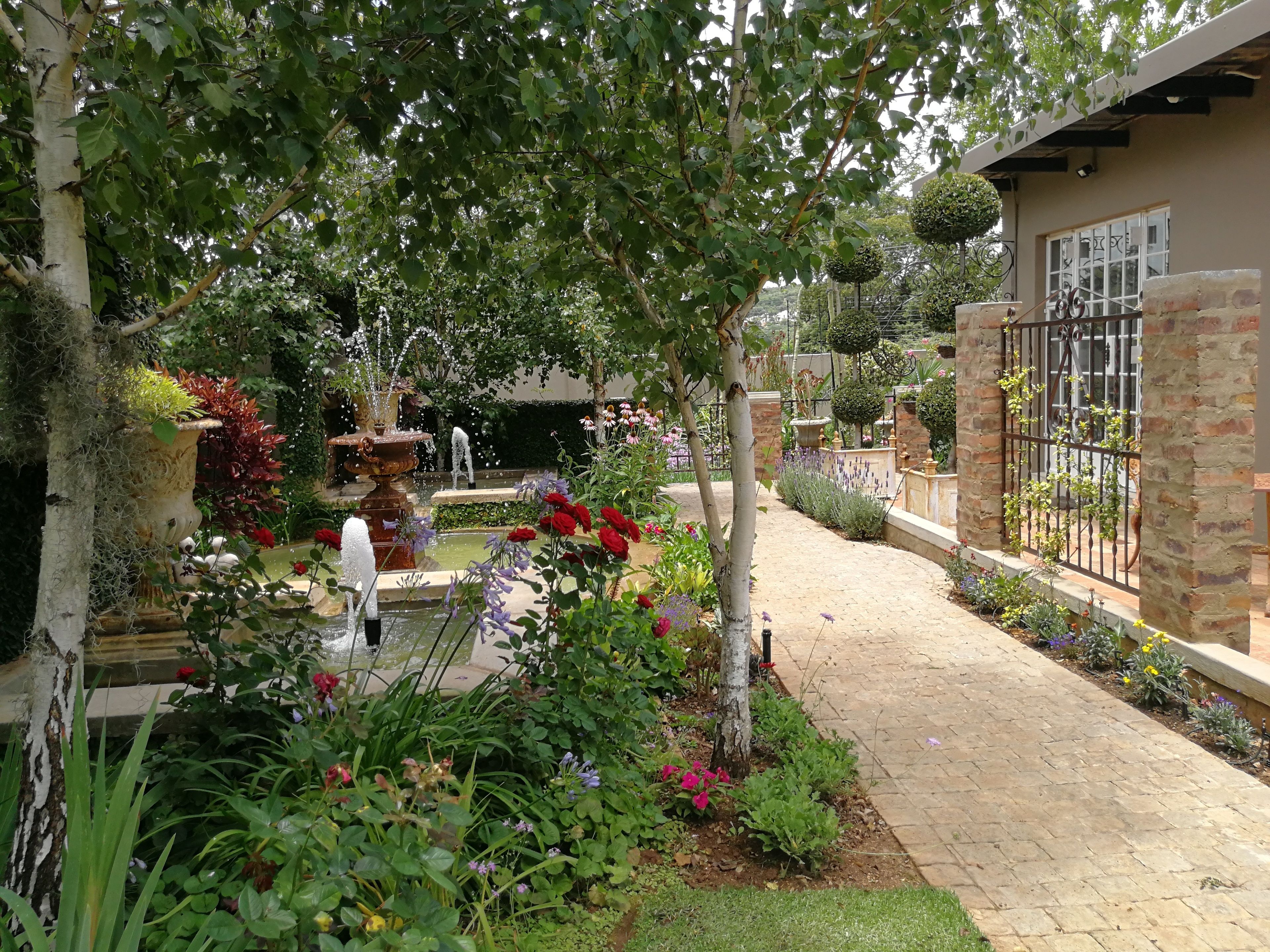 A garden with a fountain, a brick pathway, and a variety of plants and flowers.