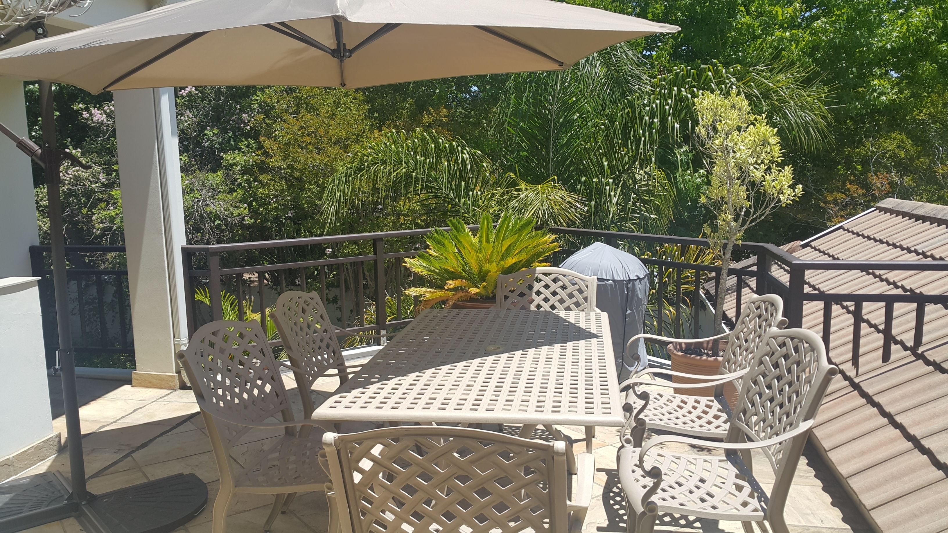 Un patio al aire libre con una mesa y sillas, rodeado por una barandilla y macetas con plantas.