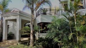 Ein zweistöckiges Haus mit Balkon, umgeben von üppiger Vegetation und Palmen.