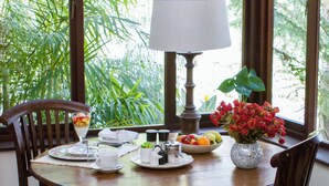 Ein Esstisch mit Stühlen, eine Lampe, eine Vase mit Blumen und eine Schale mit Obst.