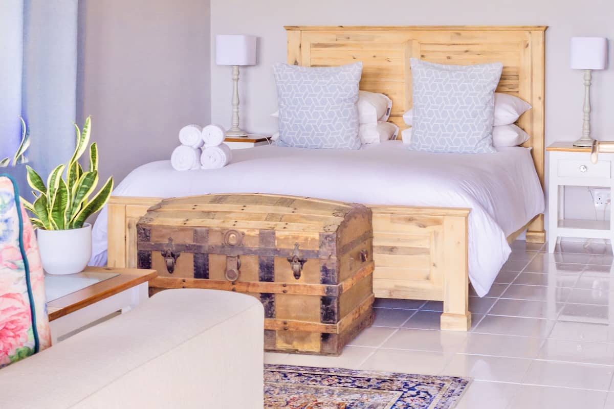 A bedroom with a wooden bed, a chest of drawers, a potted plant, and a nightstand with a lamp.