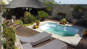 A swimming pool with lounge chairs, a thatched-roof structure, and potted plants. - Kumbaya House (Cape Town)