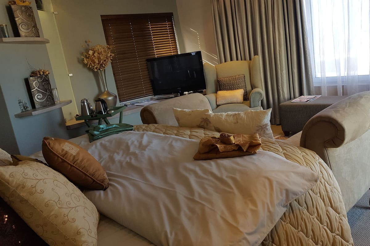 A hotel room with a large bed, two armchairs, a small table, a television, and a window with curtains.