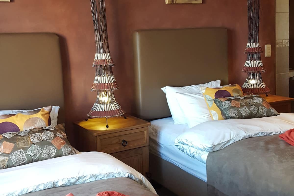 A hotel room with two beds, each with a headboard, a bedside table, and a lamp.