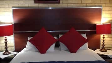 A hotel room with a wooden headboard, a bed with red and white bedding, and two bedside lamps.