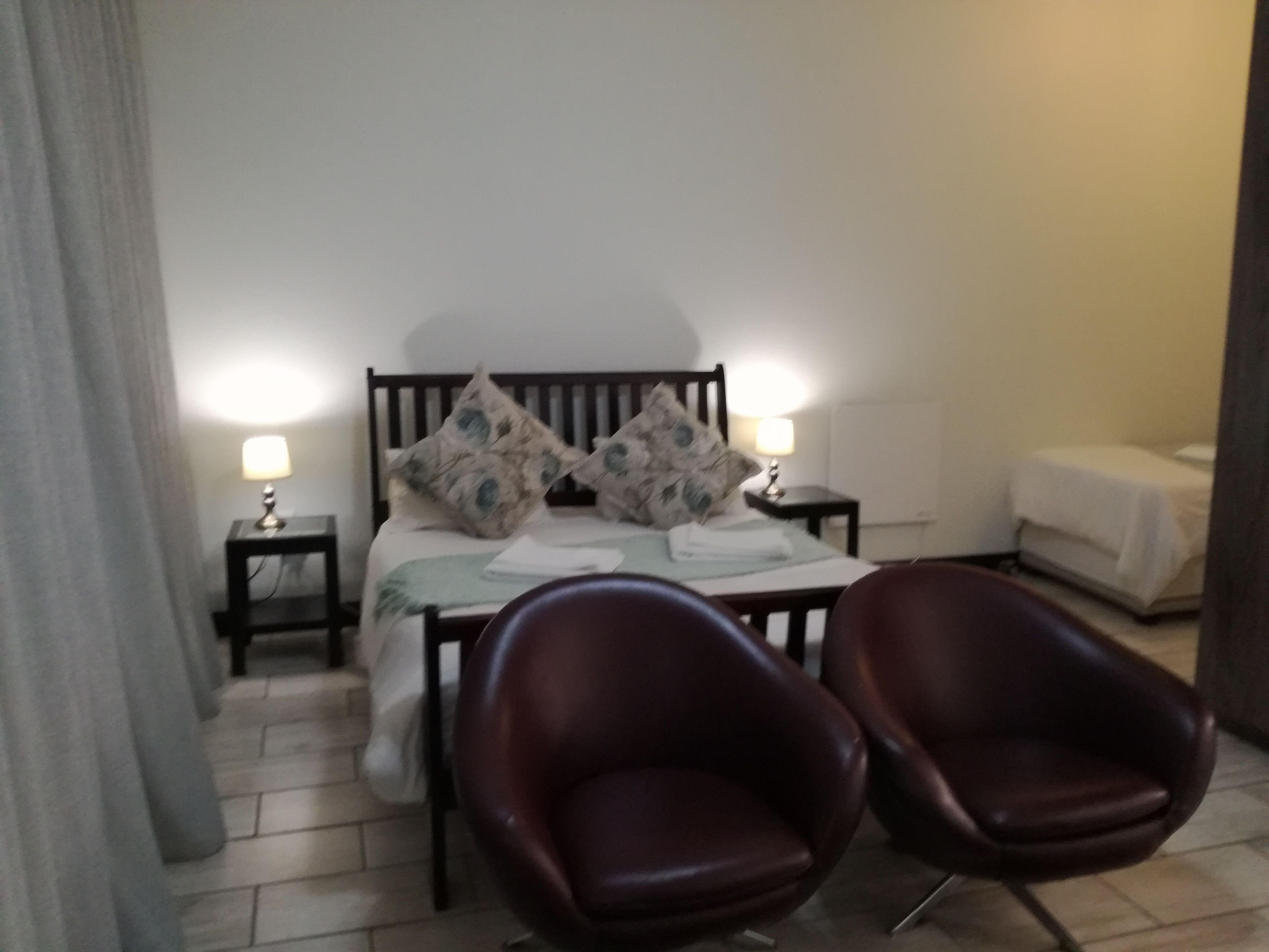 Habitación de hotel con una cama, dos mesitas de noche con lámparas, una silla y una pequeña mesita de noche con lámpara.