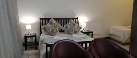 Habitación de hotel con una cama, dos mesitas de noche con lámparas, una silla y una pequeña mesita de noche con lámpara.