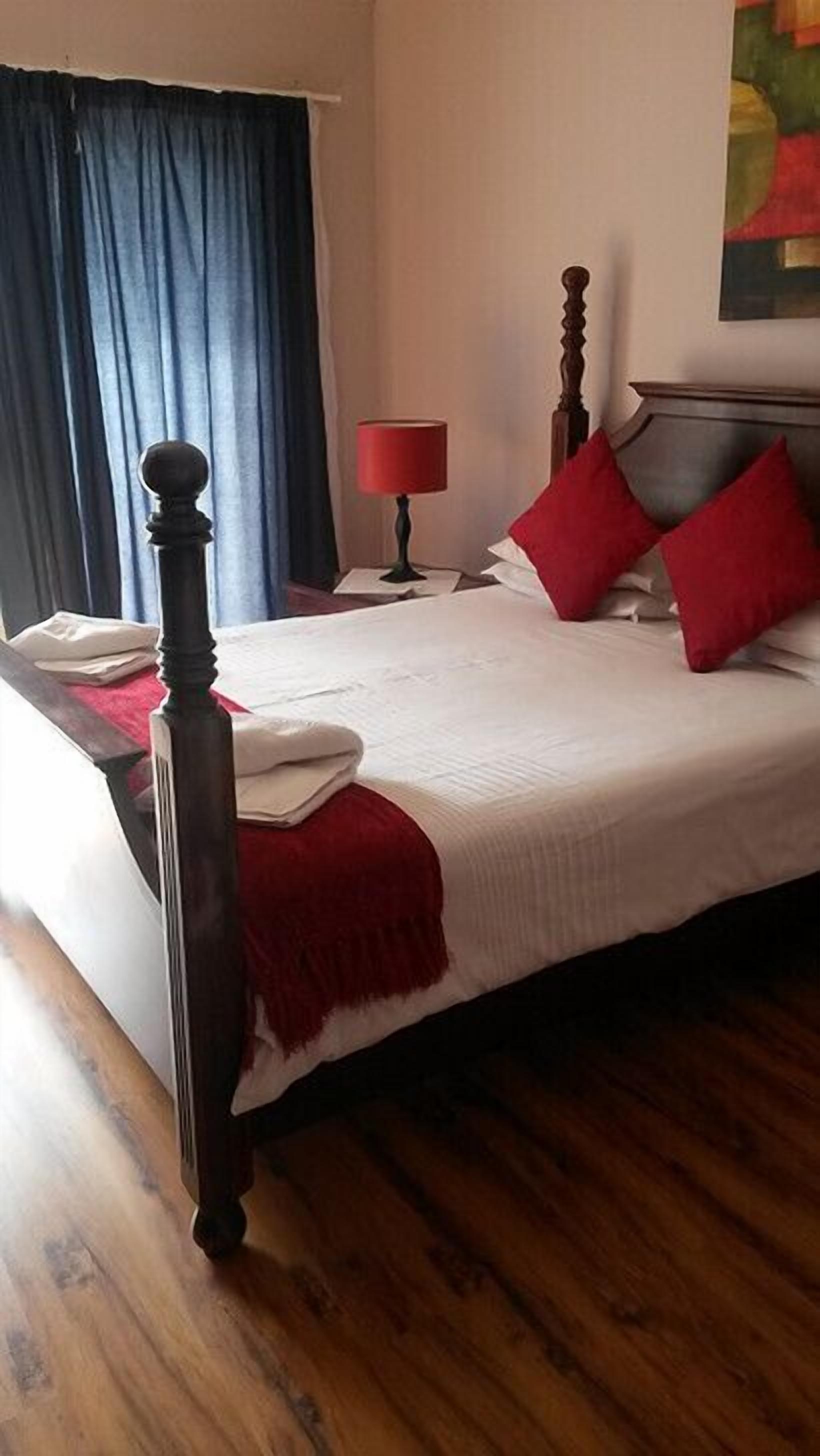 A neatly made bed with a wooden headboard, a red lamp on a bedside table, and a blue curtain.