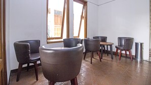 A room with six chairs arranged around a small table, large windows with wooden frames, and a tiled floor.