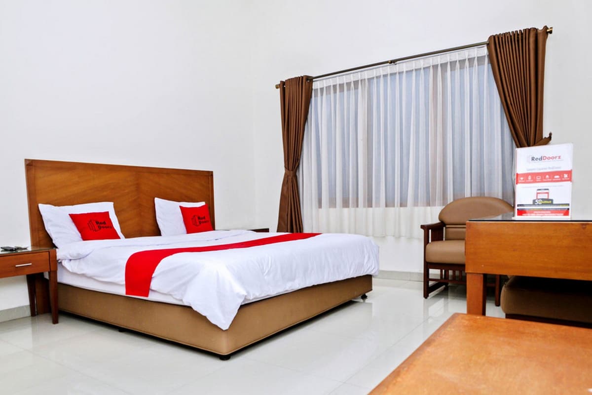 Habitación de hotel con cama, escritorio, silla y ventana con cortinas.