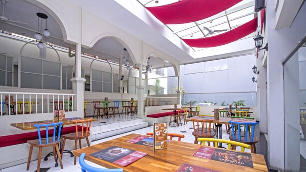 A spacious restaurant with high ceilings, wooden tables, and colorful chairs.