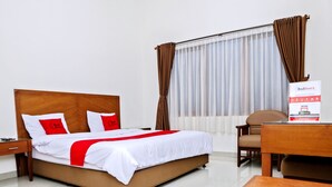 A hotel room with a bed, a desk, a chair, and a window with curtains.