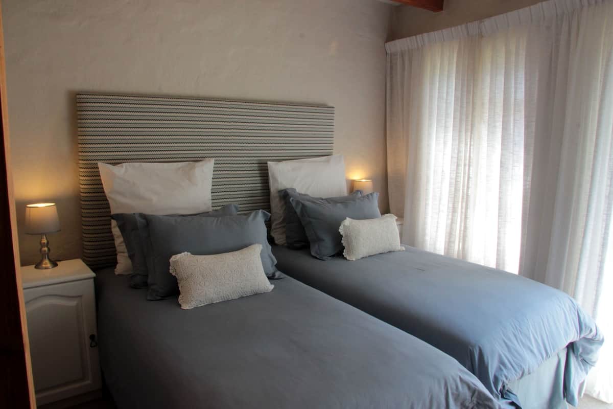 Una cama doble con cabecera a rayas, dos mesitas de noche con lámparas y una ventana con cortinas translúcidas.