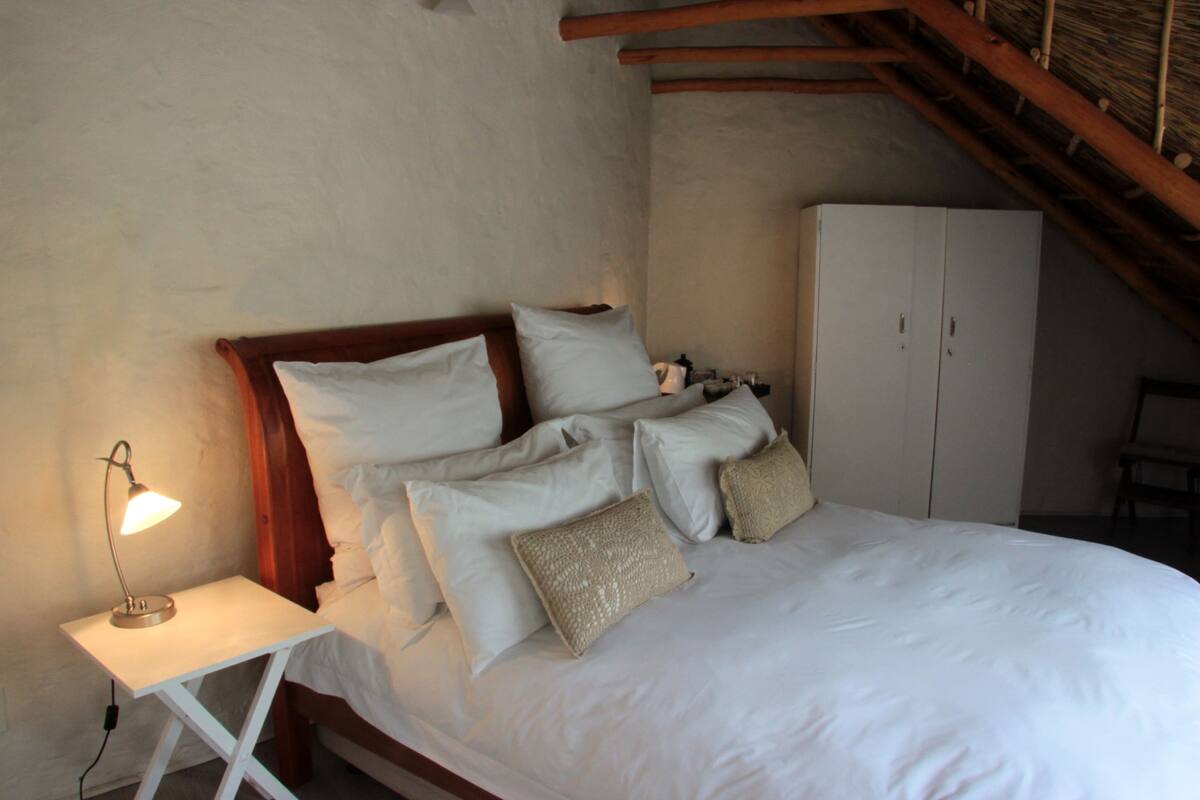 Un dormitorio con cama, almohadas, mesita de noche con lámpara y armario.