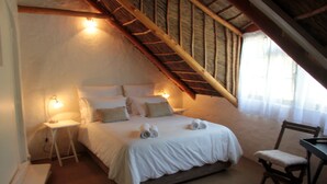 Ein Schlafzimmer mit Bett, Nachttischen, einem Sessel und einer schrägen Decke.