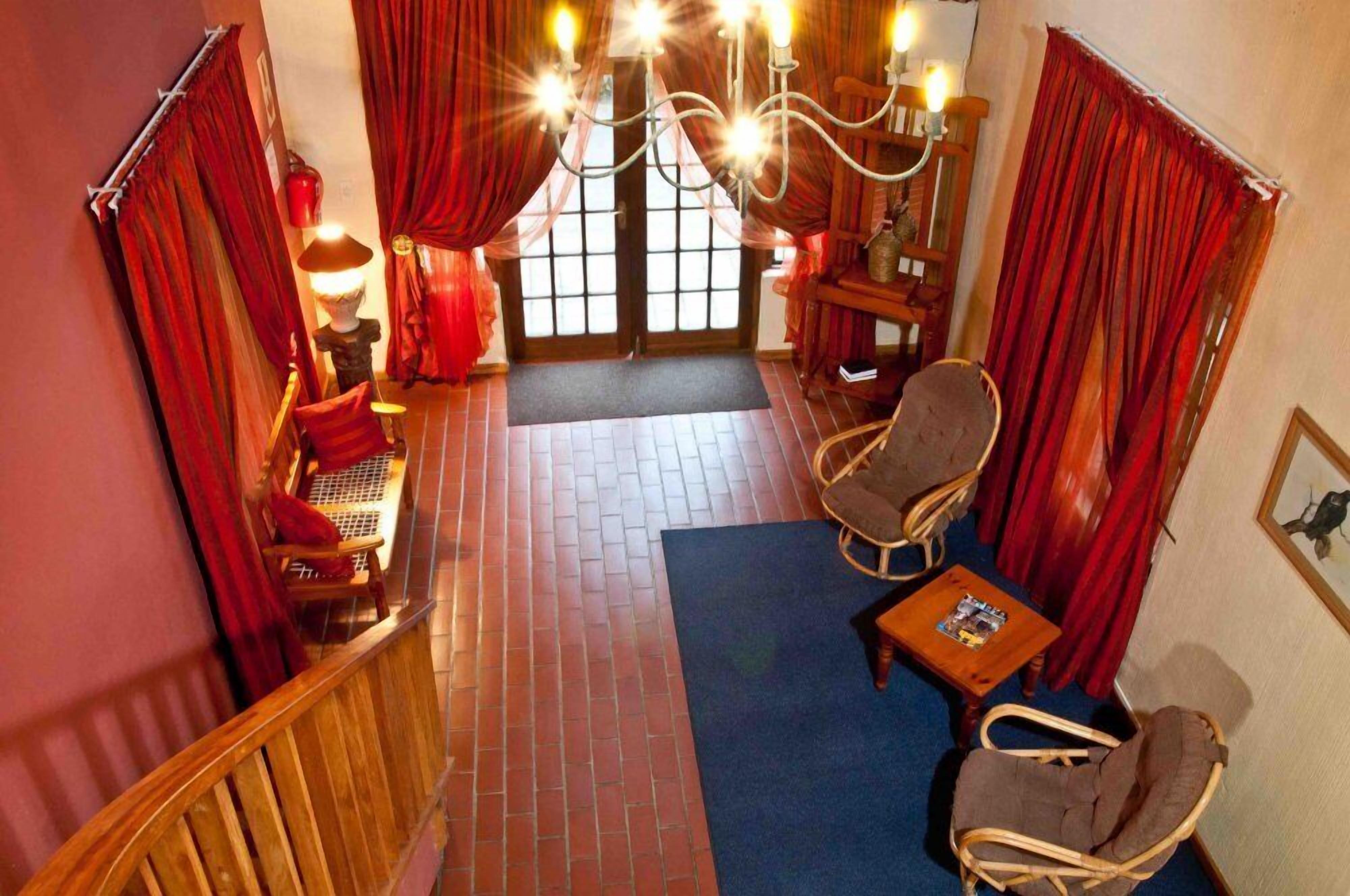 Une pièce chaleureuse avec un sol en briques, des rideaux rouges, un banc en bois, une chaise en osier et un lustre.