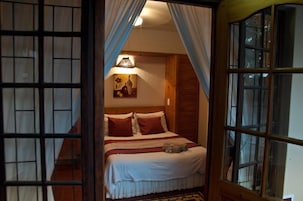 A bedroom with a wooden headboard, a bed with red and white bedding, a lamp, and a painting on the wall.