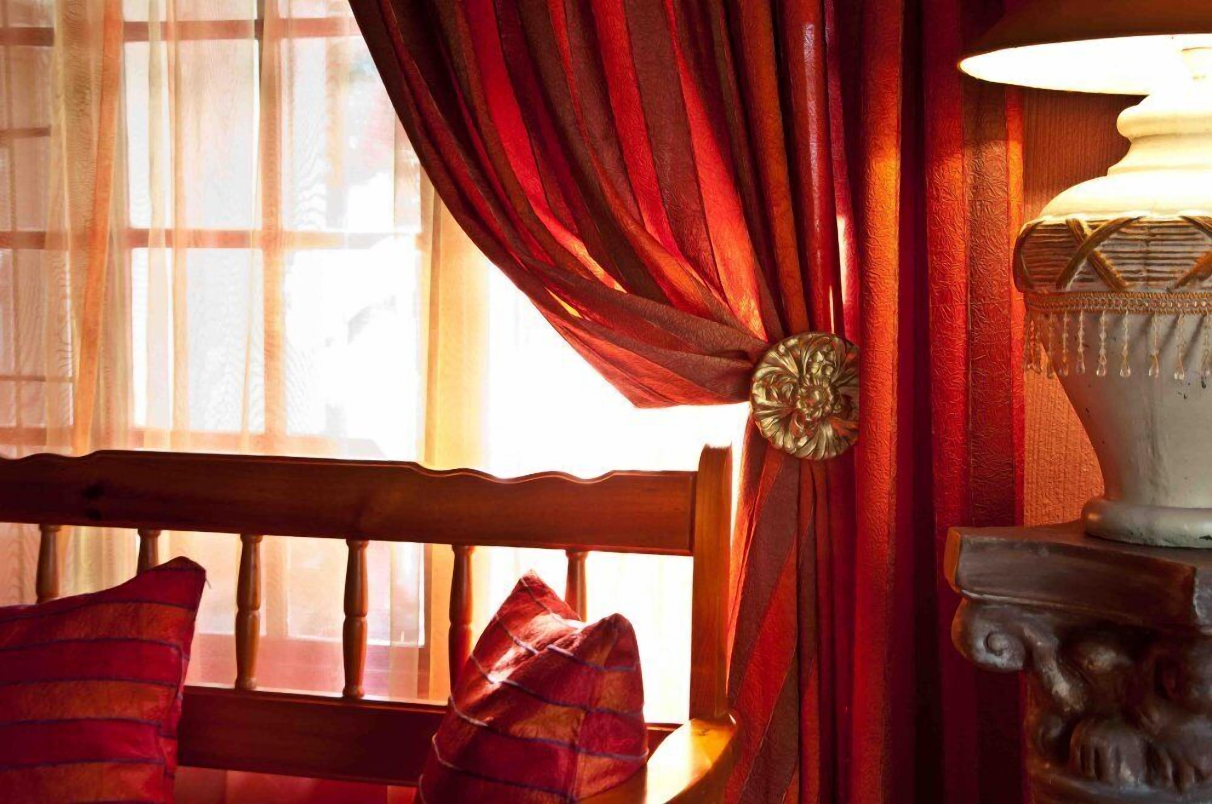 Ein Zimmer mit einer hölzernen Bank, roten Vorhängen und einer Lampe auf einem Sockel.
