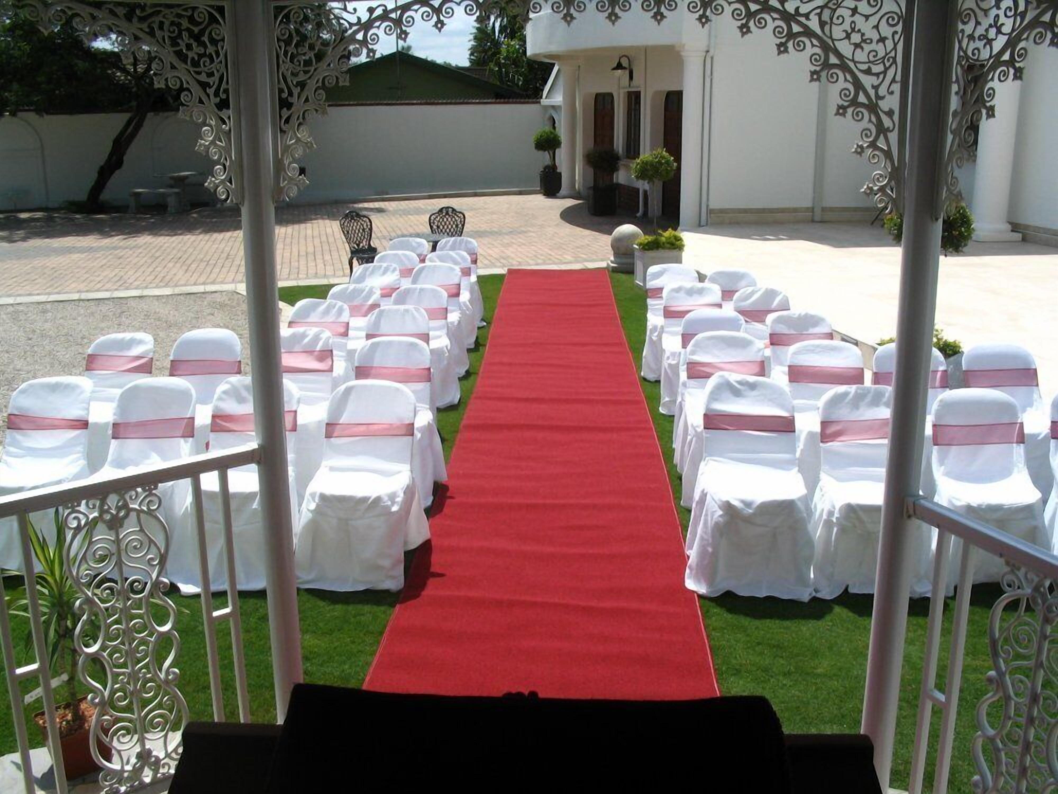 An outdoor wedding aisle with white chairs and a red carpet.