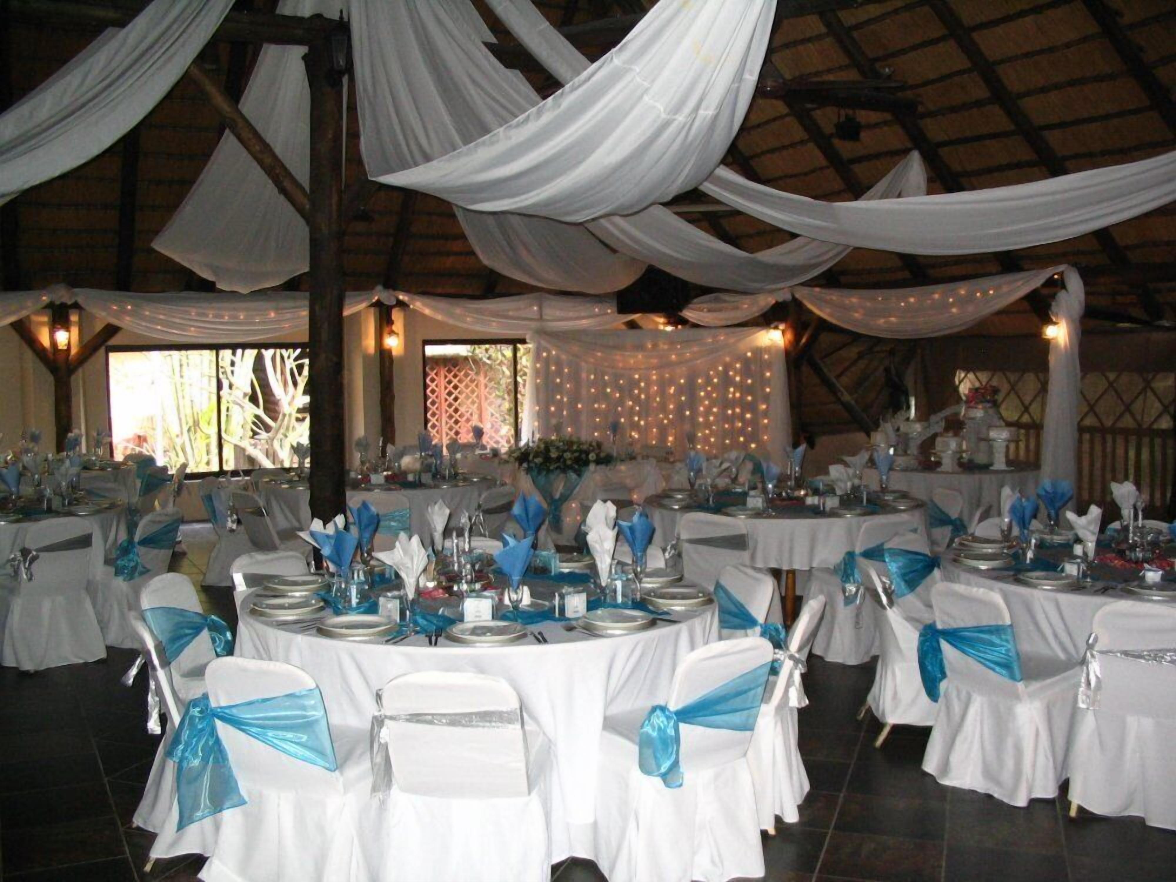 Un salón de banquetes con mesas redondas cubiertas con manteles blancos y fajas azules, dispuesto para un evento formal.