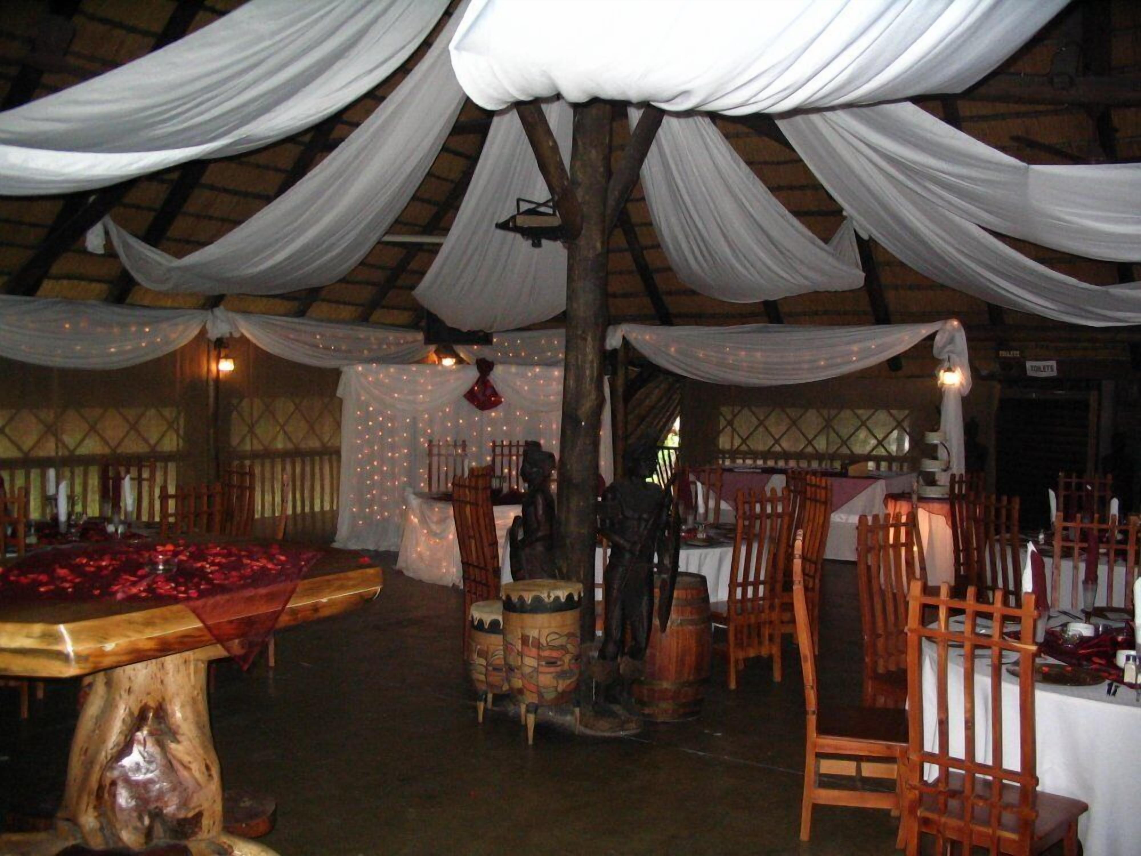 A rustic venue with wooden furniture, white drapes, and a central table with red decorations.
