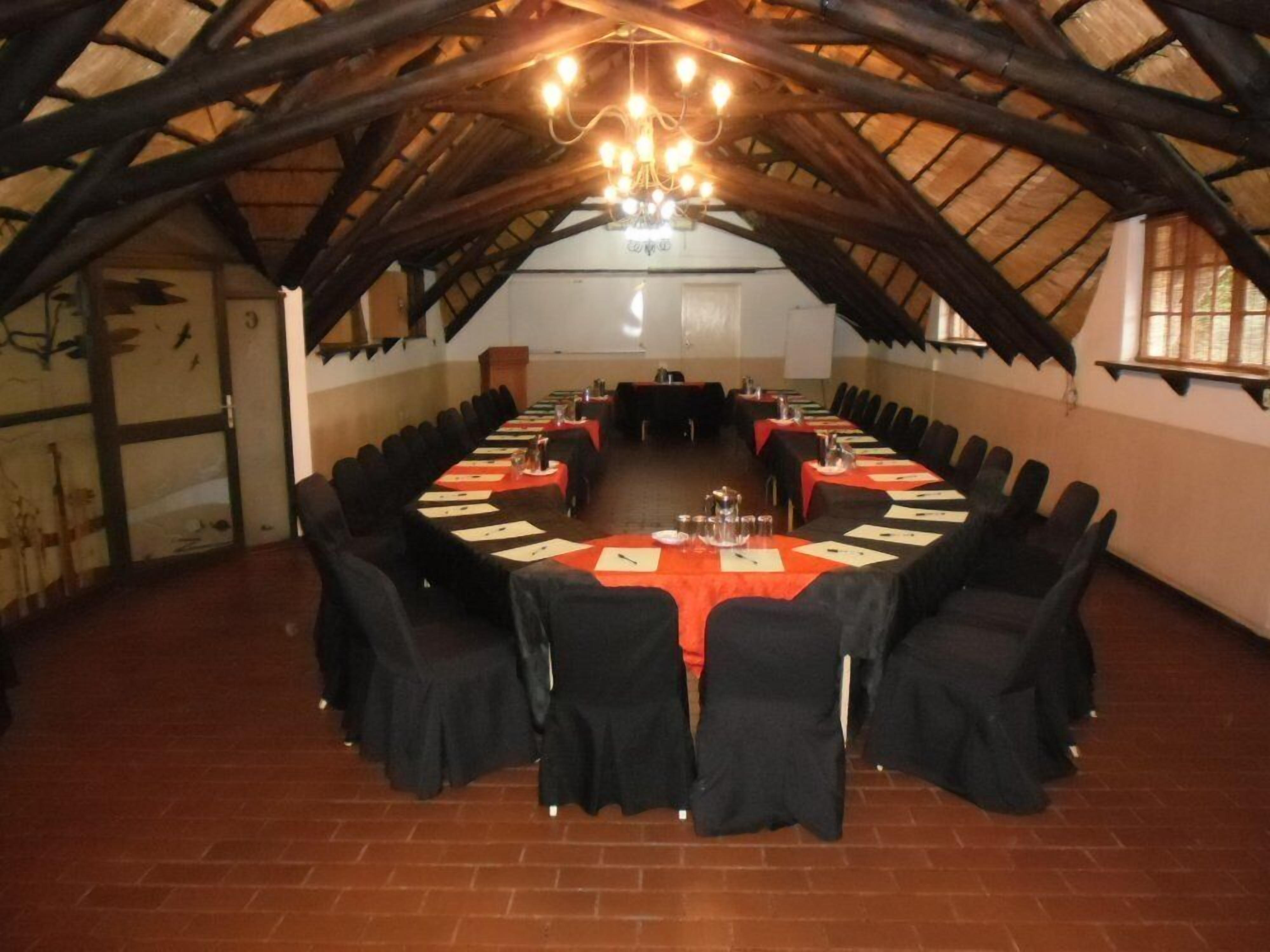 A conference room with a long table set for meetings, surrounded by chairs, under a high ceiling with exposed beams.