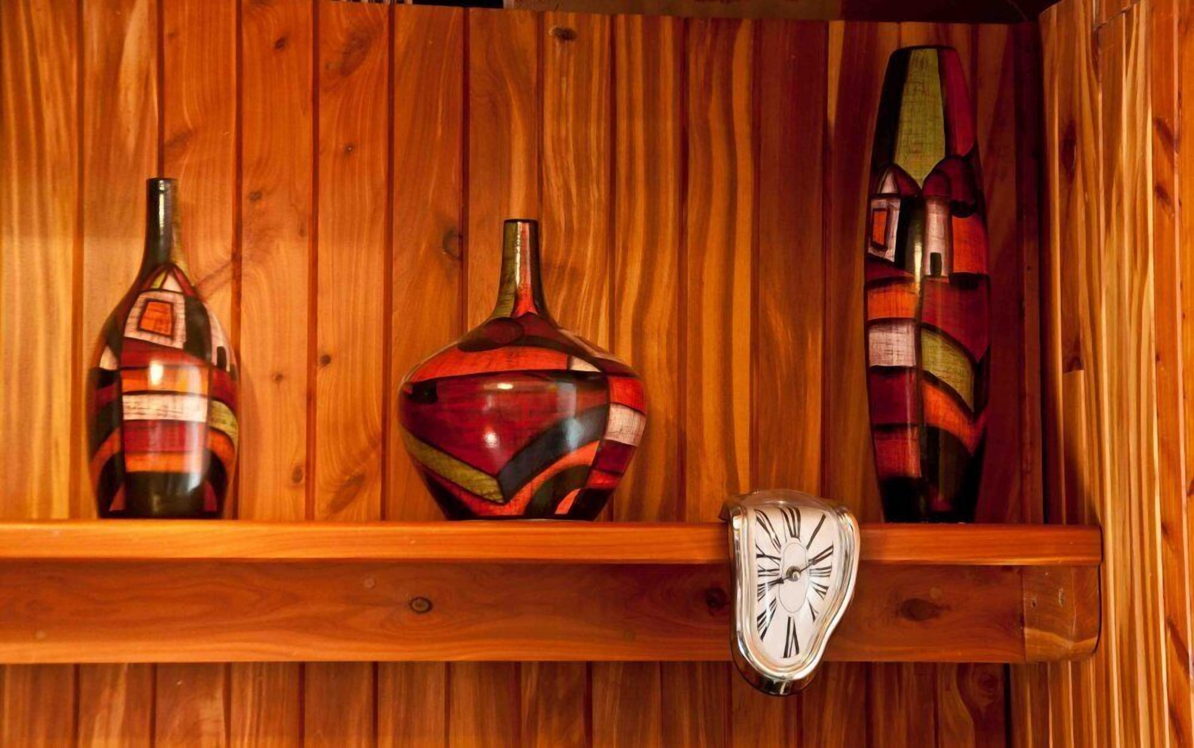 A wooden shelf with three decorative vases and a clock.