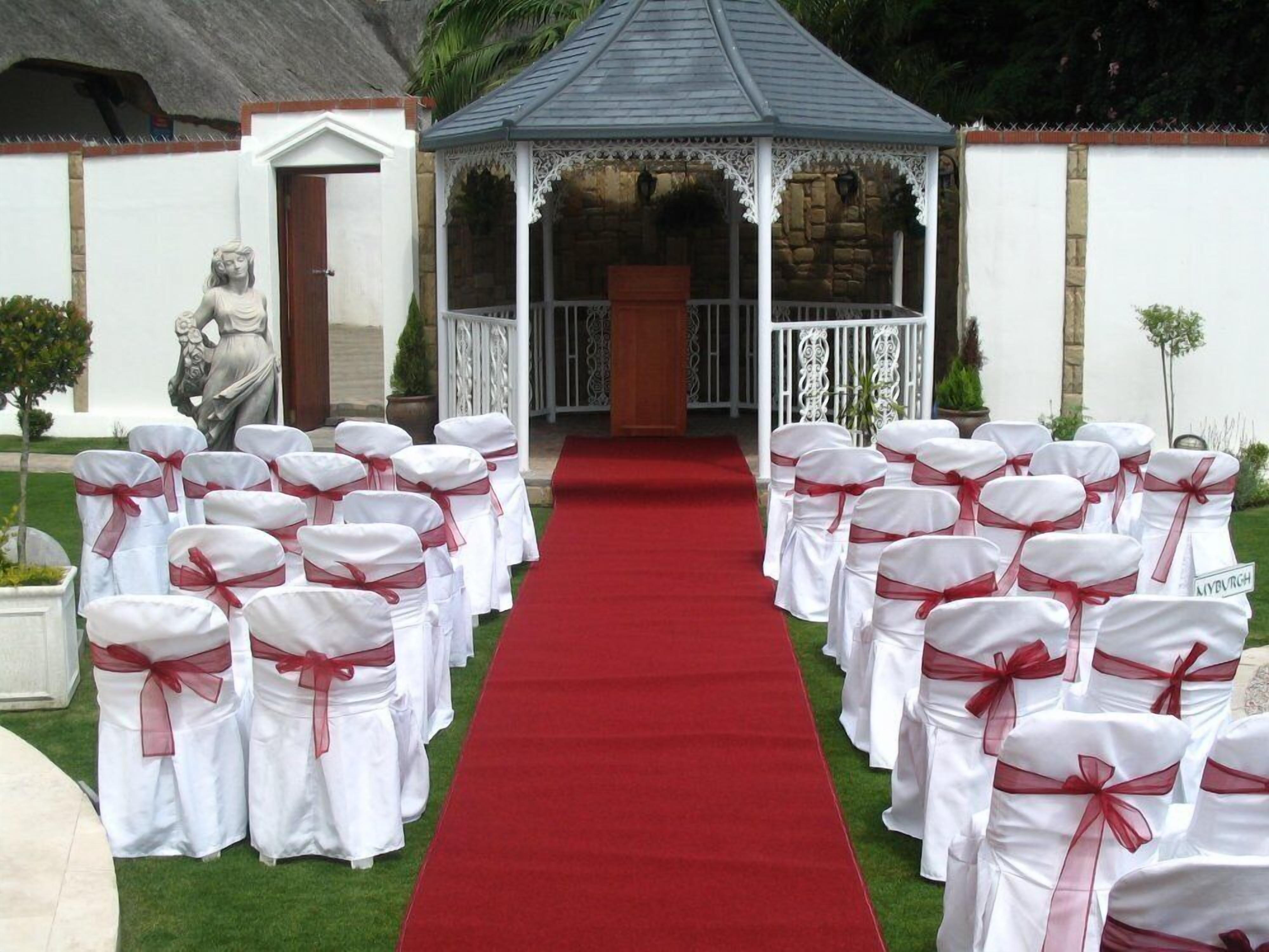 A red carpet aisle leading to a gazebo with white chairs on either side, each with a red sash.