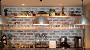 A kitchen with a brick wall, shelves with glassware, a coffee machine, and a clock. - Phoenix Lodge and Waterside Accommodation (Knysna)