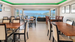 A modern dining area with tables and chairs, large windows with a view of a body of water and a bridge, and green ambient lighting. - Phoenix Lodge and Waterside Accommodation (Knysna)