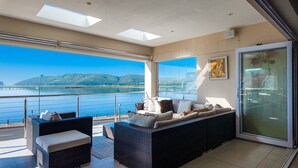 A balcony with wicker furniture and a view of a body of water and hills. - Phoenix Lodge and Waterside Accommodation (Knysna)