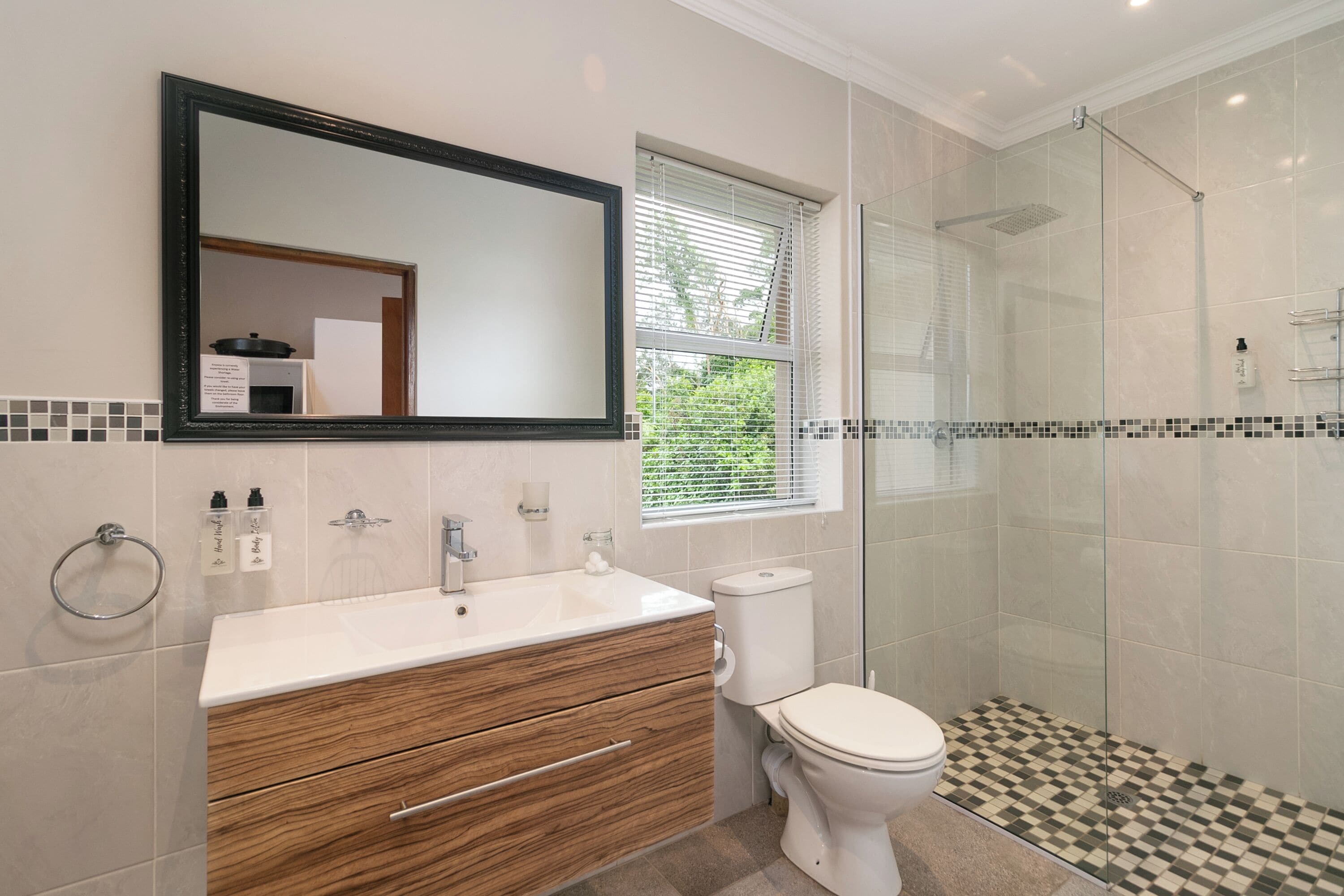 A bathroom with a white sink, wooden vanity, a toilet, and a glass-enclosed shower.