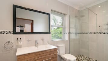 A bathroom with a white sink, wooden vanity, a toilet, and a glass-enclosed shower.