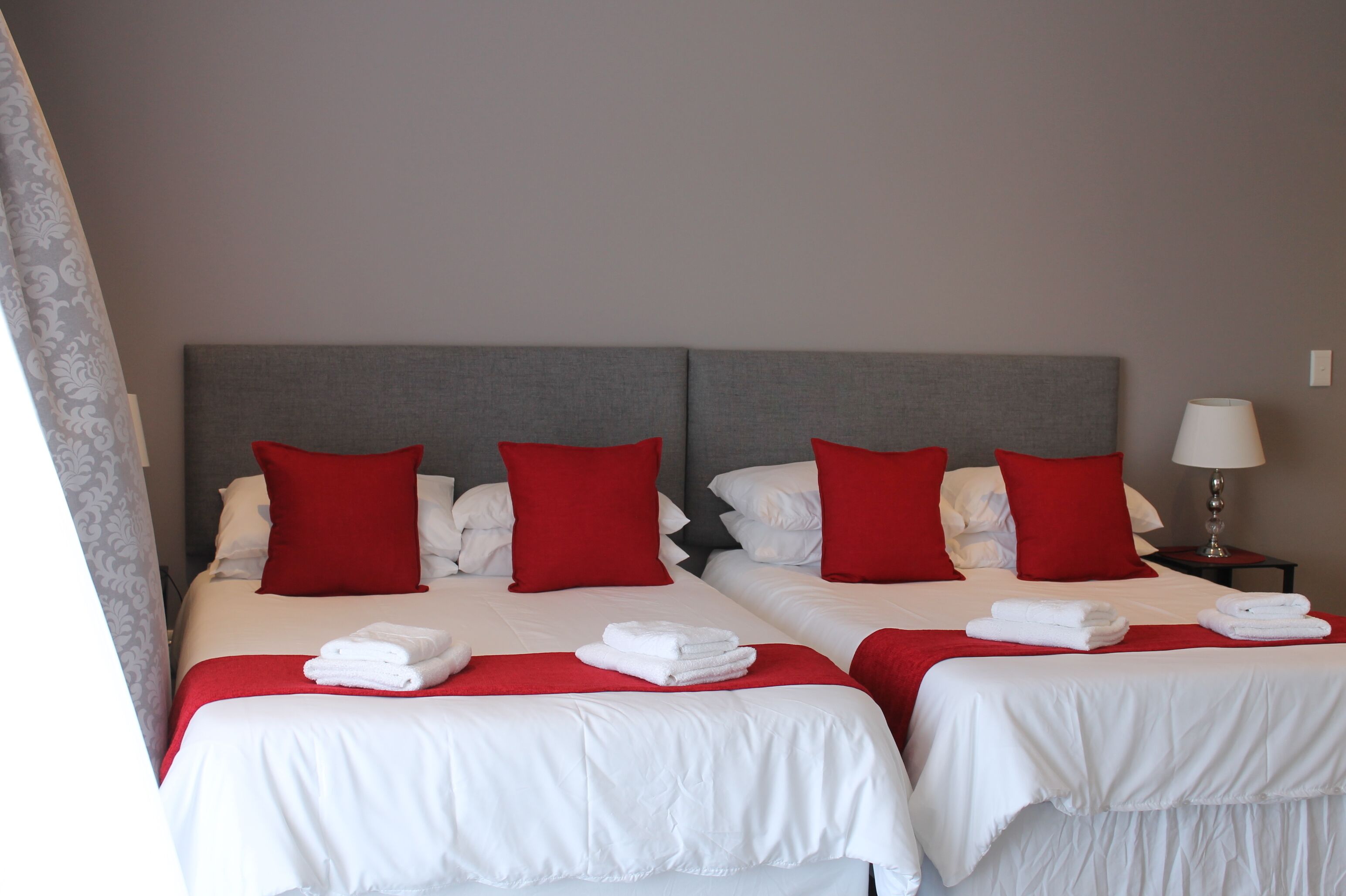 A hotel room with two beds, each with white bedding and red pillows. There are folded towels on the beds.