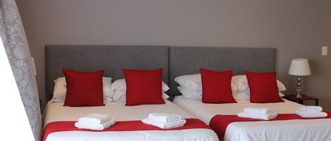 A hotel room with two beds, each with white bedding and red pillows. There are folded towels on the beds.