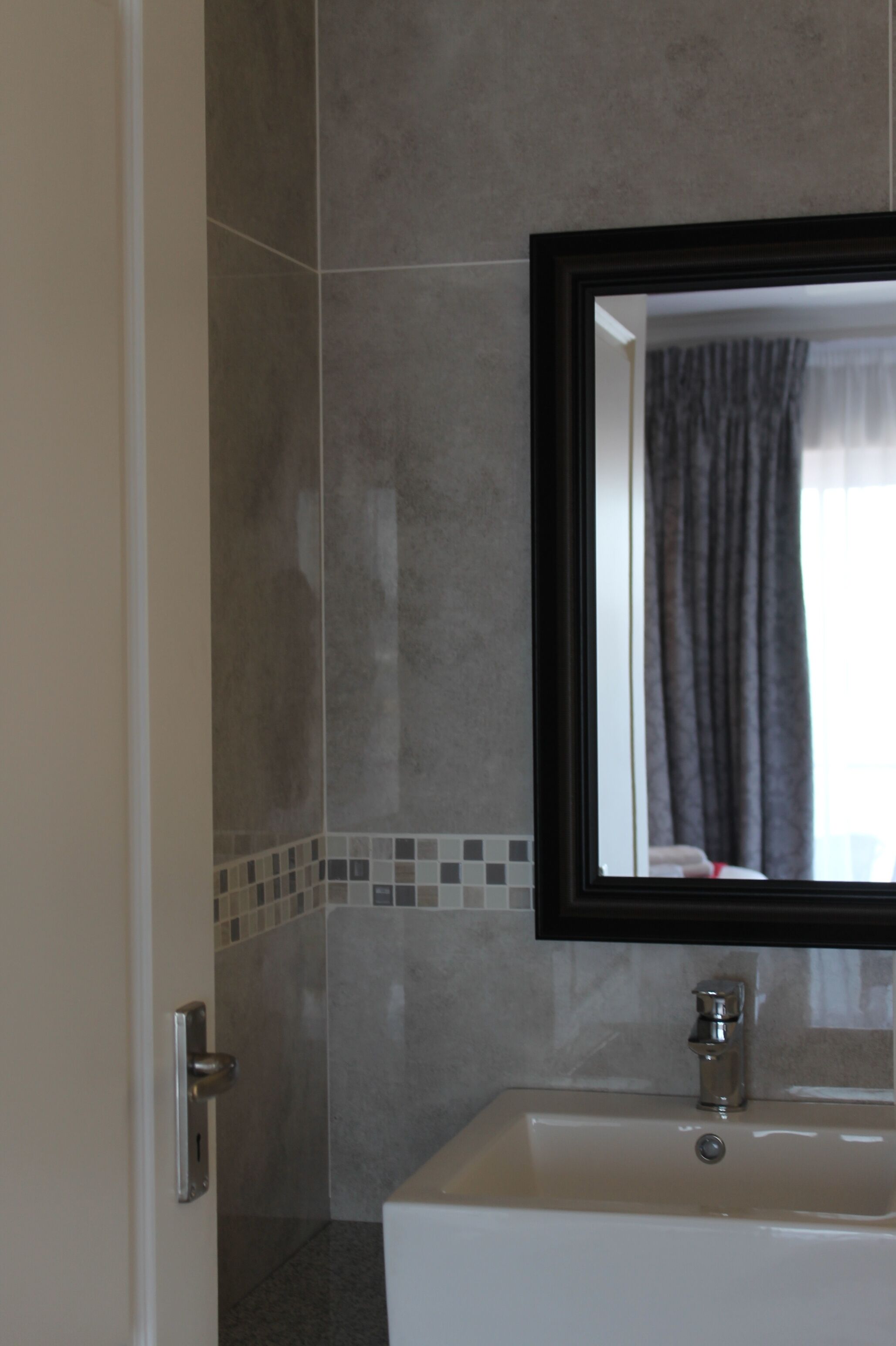 Un baño con lavamanos blanco, un espejo y zona de ducha.