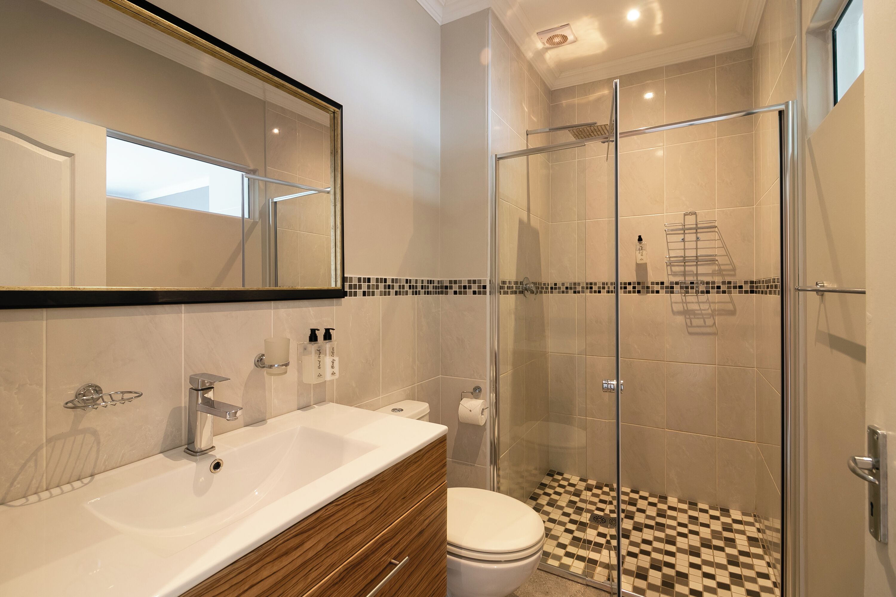 A modern bathroom with a glass-enclosed shower, a white sink, and a checkered floor.