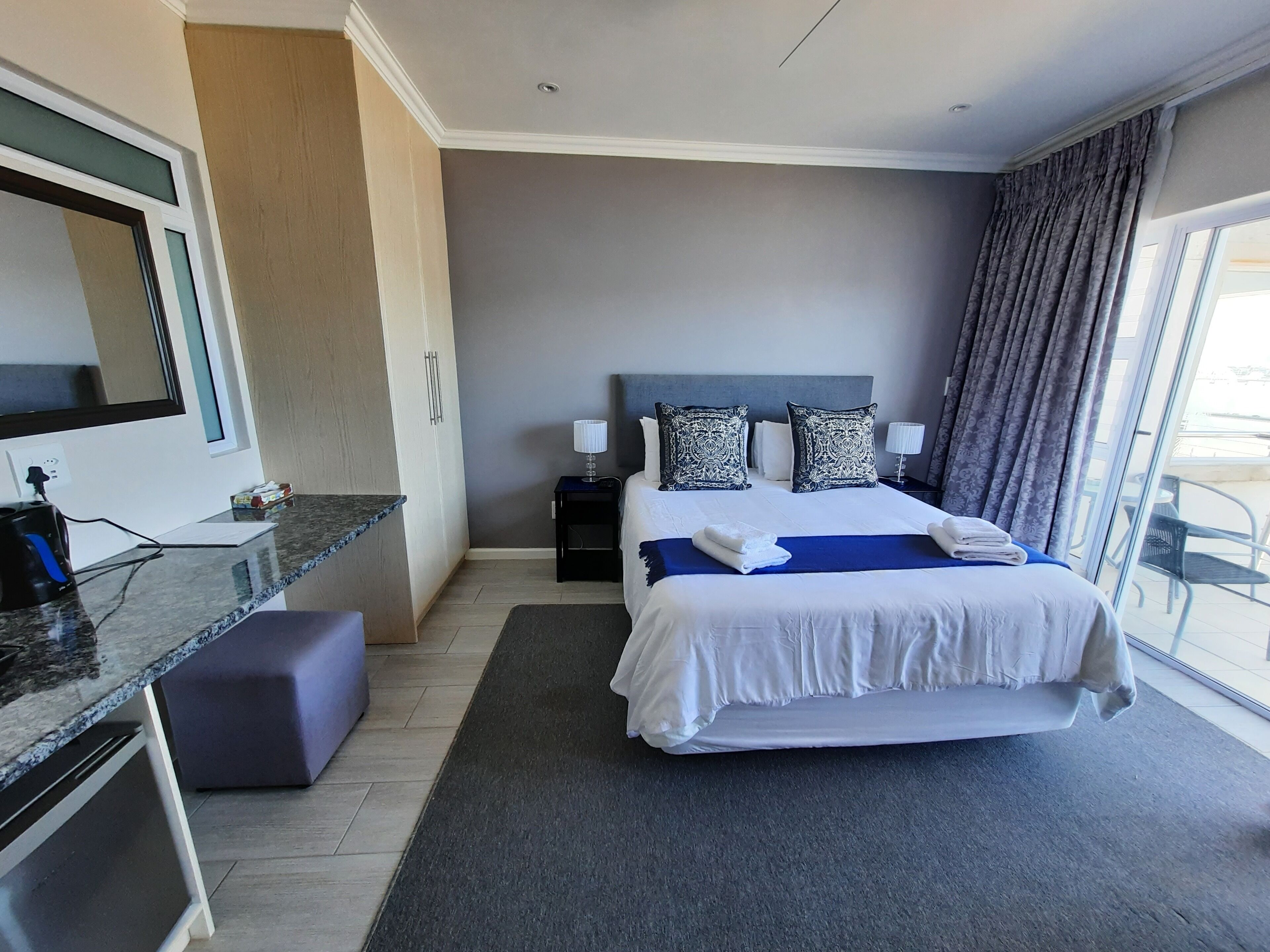 A hotel room with a large bed, a desk, a chair, a small table, and a window with curtains.