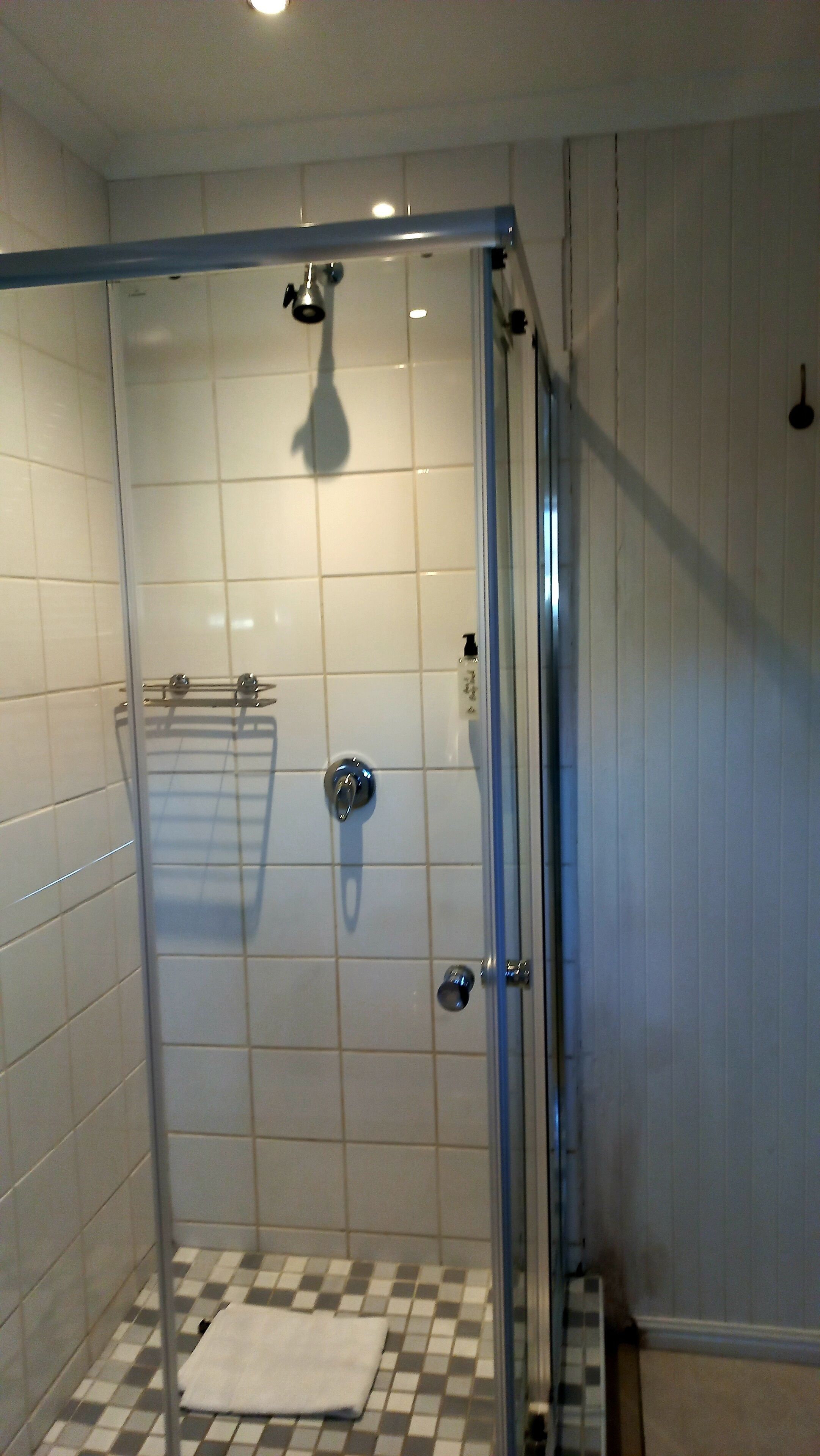 A shower with a glass door, white tiled walls, and a checkered floor.
