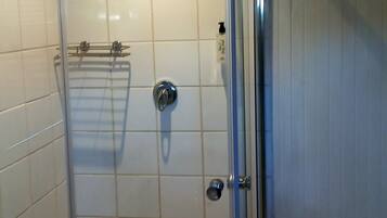 A shower with a glass door, white tiled walls, and a checkered floor.