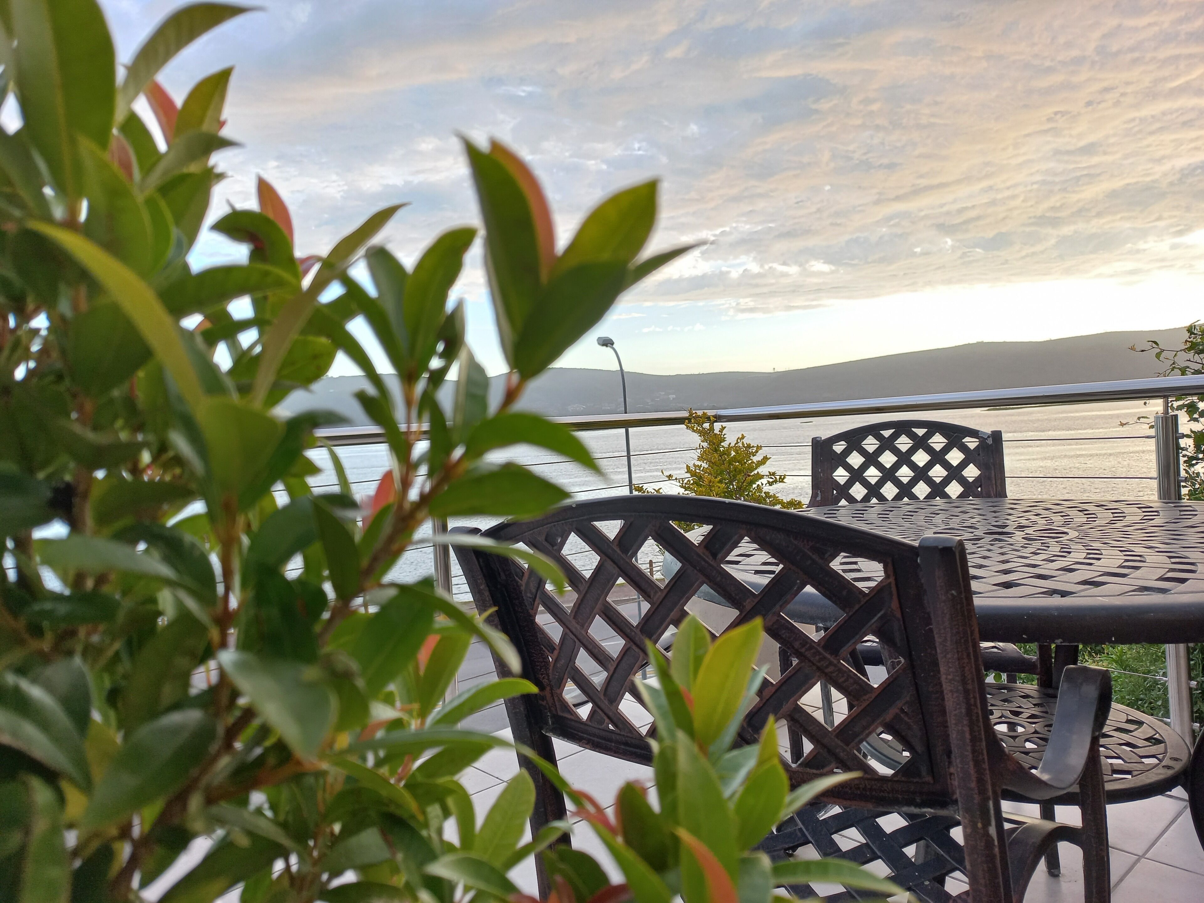 A table and chairs with a metal lattice design, overlooking a body of water with a distant landmass.