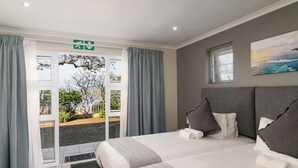 A hotel room with a large bed, grey curtains, a view of the outdoors, and a painting on the wall. - Phoenix Lodge and Waterside Accommodation (Knysna)