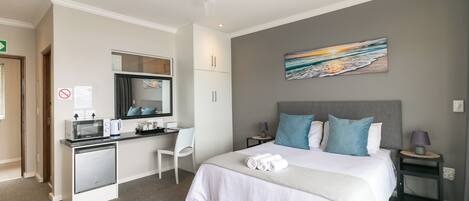 A hotel room with a bed, a desk with a computer, a chair, a microwave, and a painting on the wall.