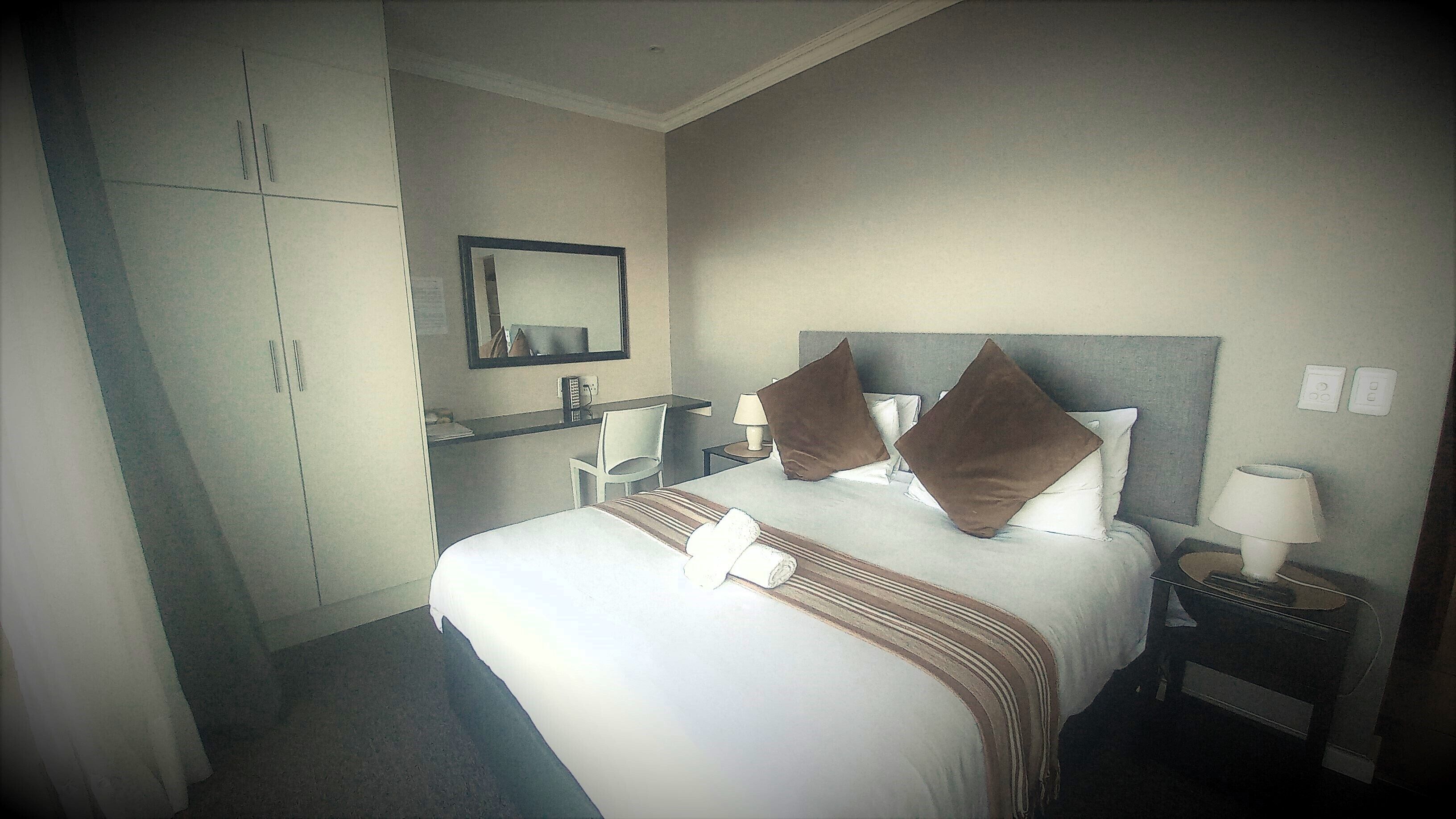 Une chambre d’hôtel avec un grand lit, un bureau, une chaise, une armoire et un miroir.