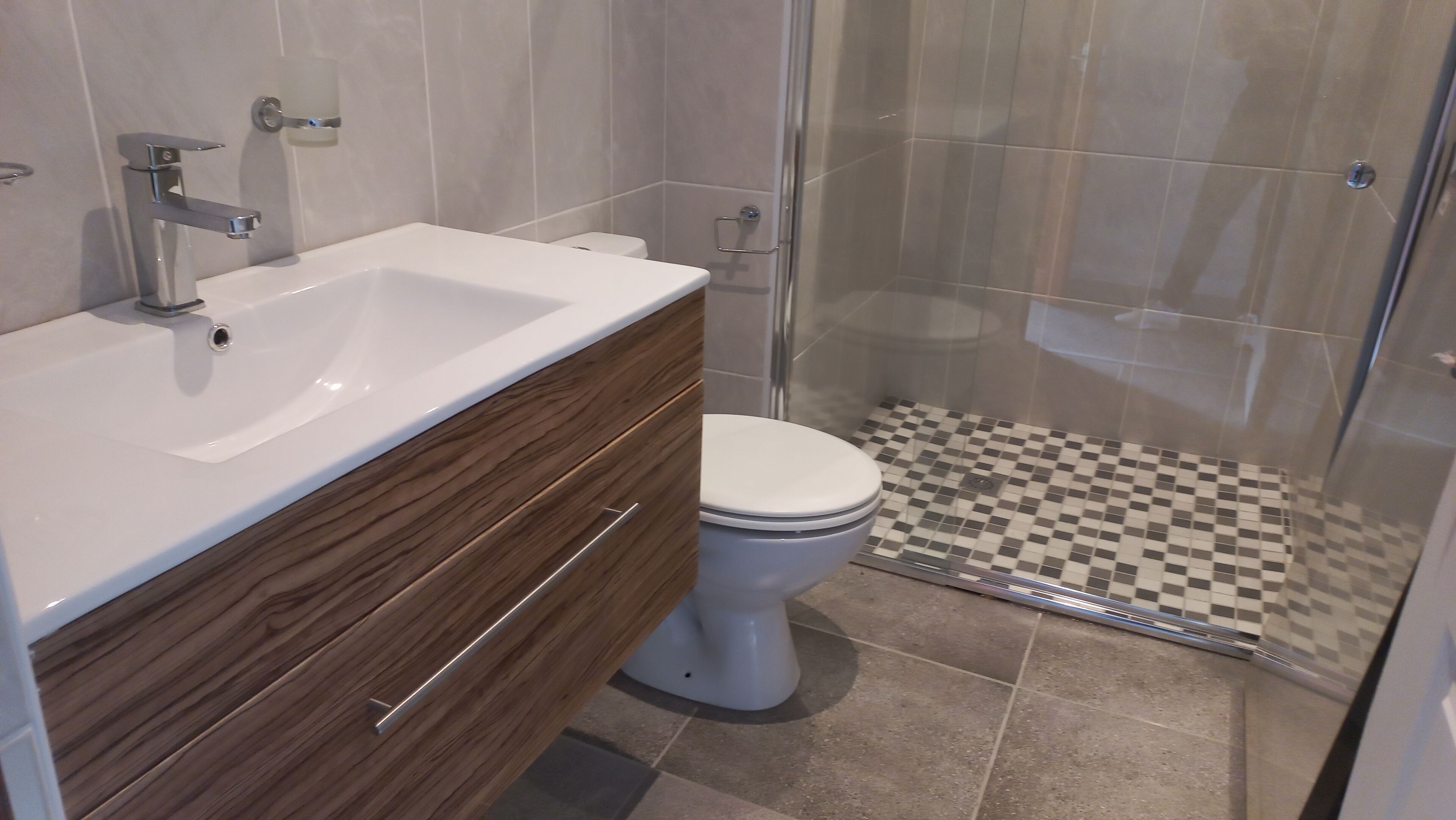 Un baño con lavamanos blanco, tocador de madera, inodoro y ducha con azulejos a cuadros.