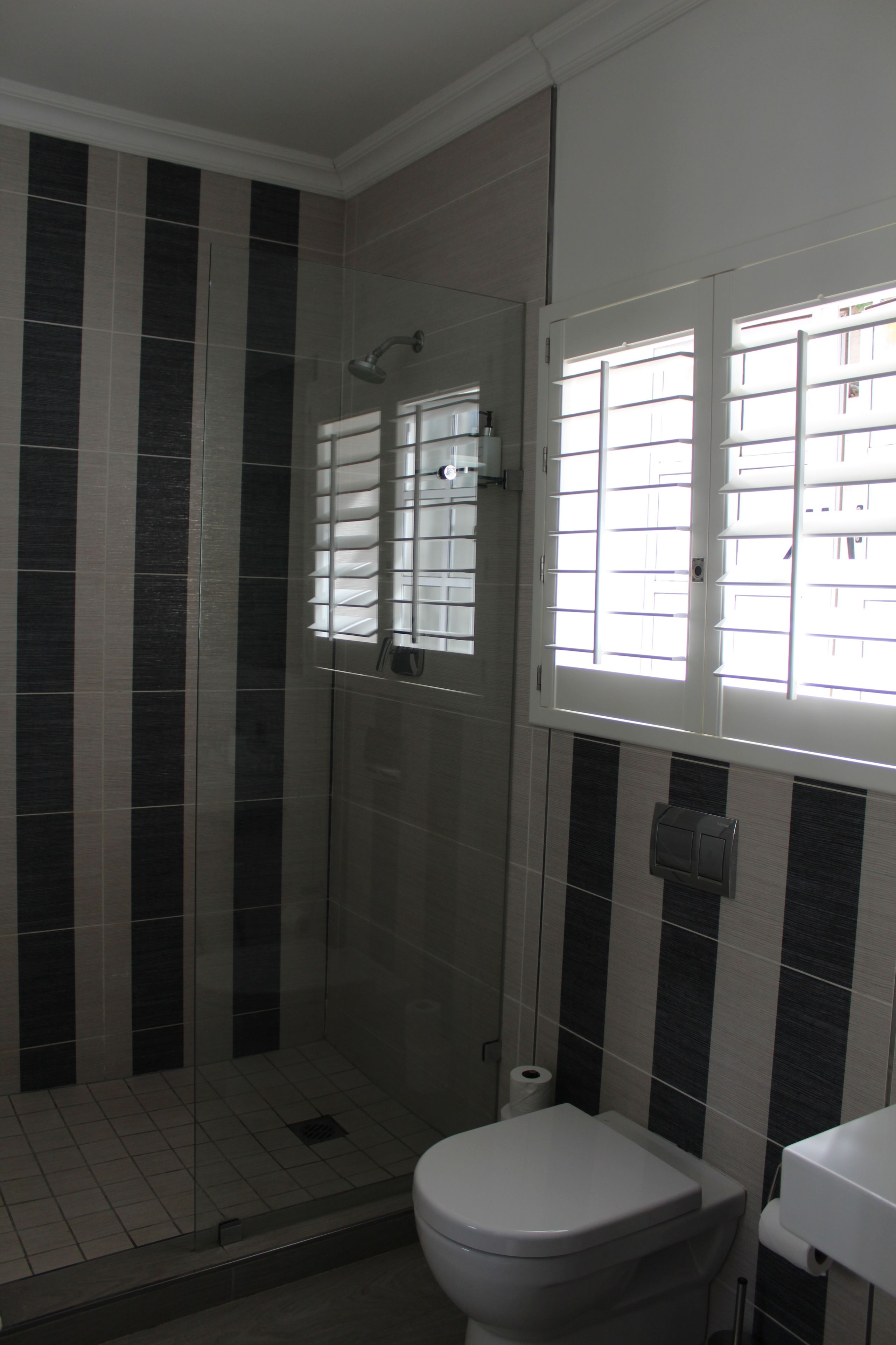 A bathroom with a toilet, a shower, and a window with blinds.