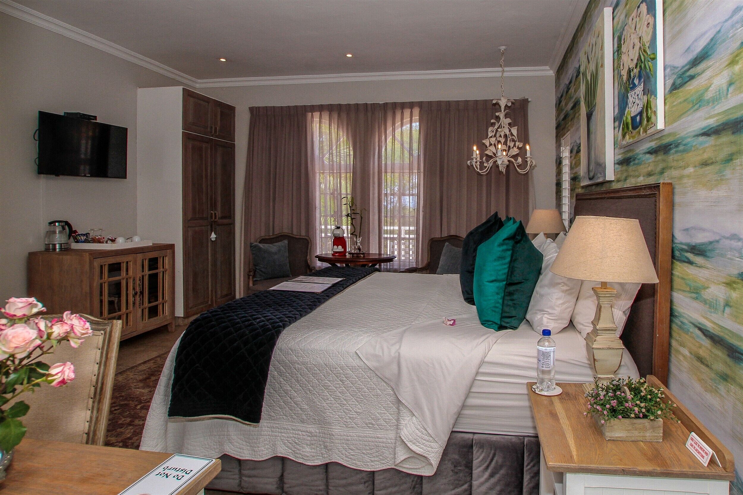 A hotel room with a large bed, a bedside table with a lamp, a TV mounted on the wall, and a painting on the wall.