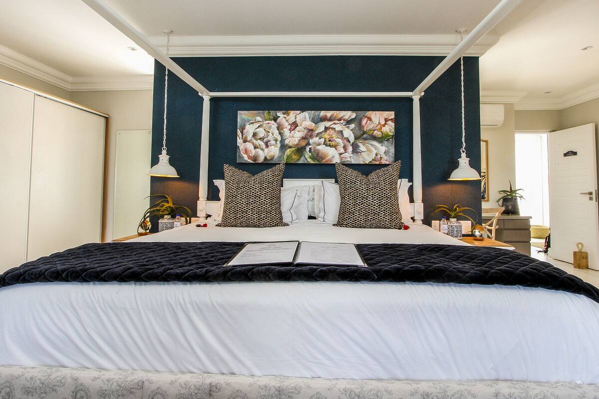 Ein Schlafzimmer mit einem großen Bett, einer dunkelblauen Akzentwand und einem floralen Gemälde darüber.