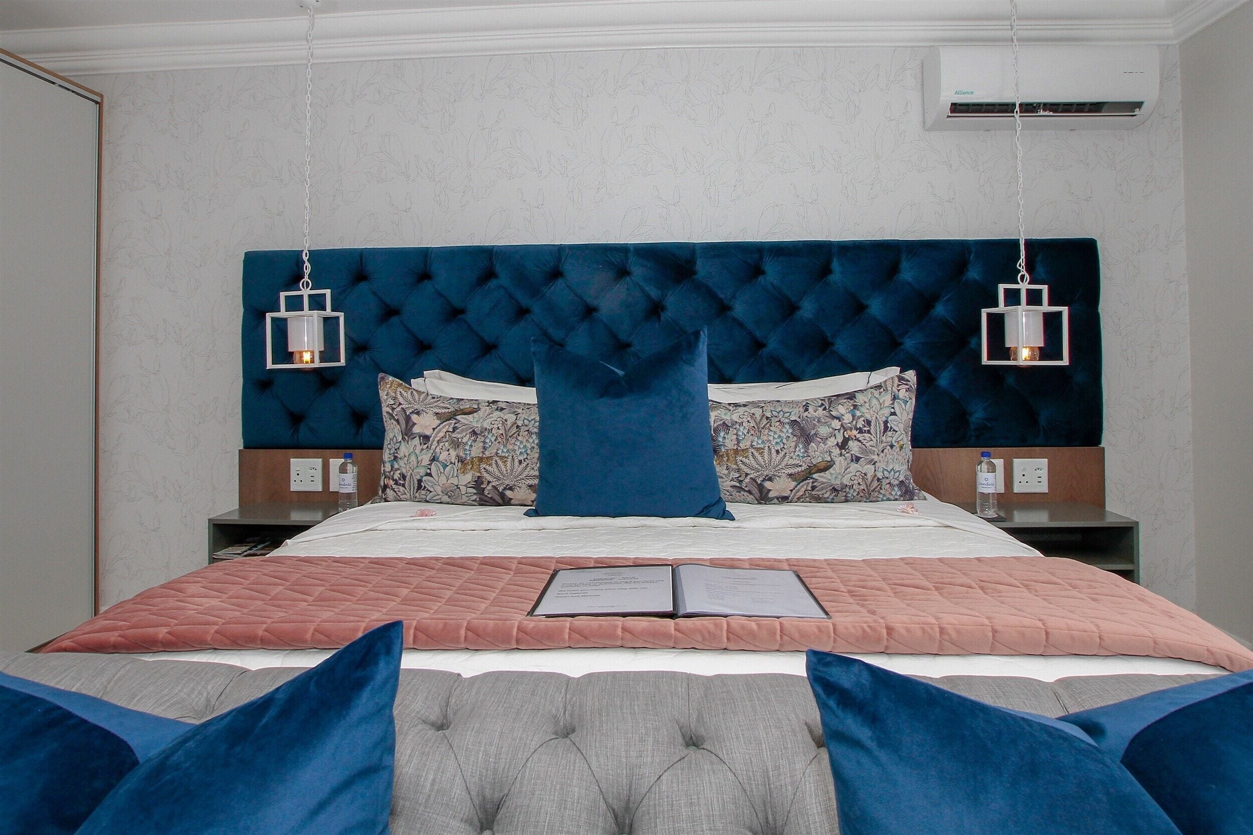 A neatly made bed with a blue headboard, two bedside tables, and a nightstand with a lamp.